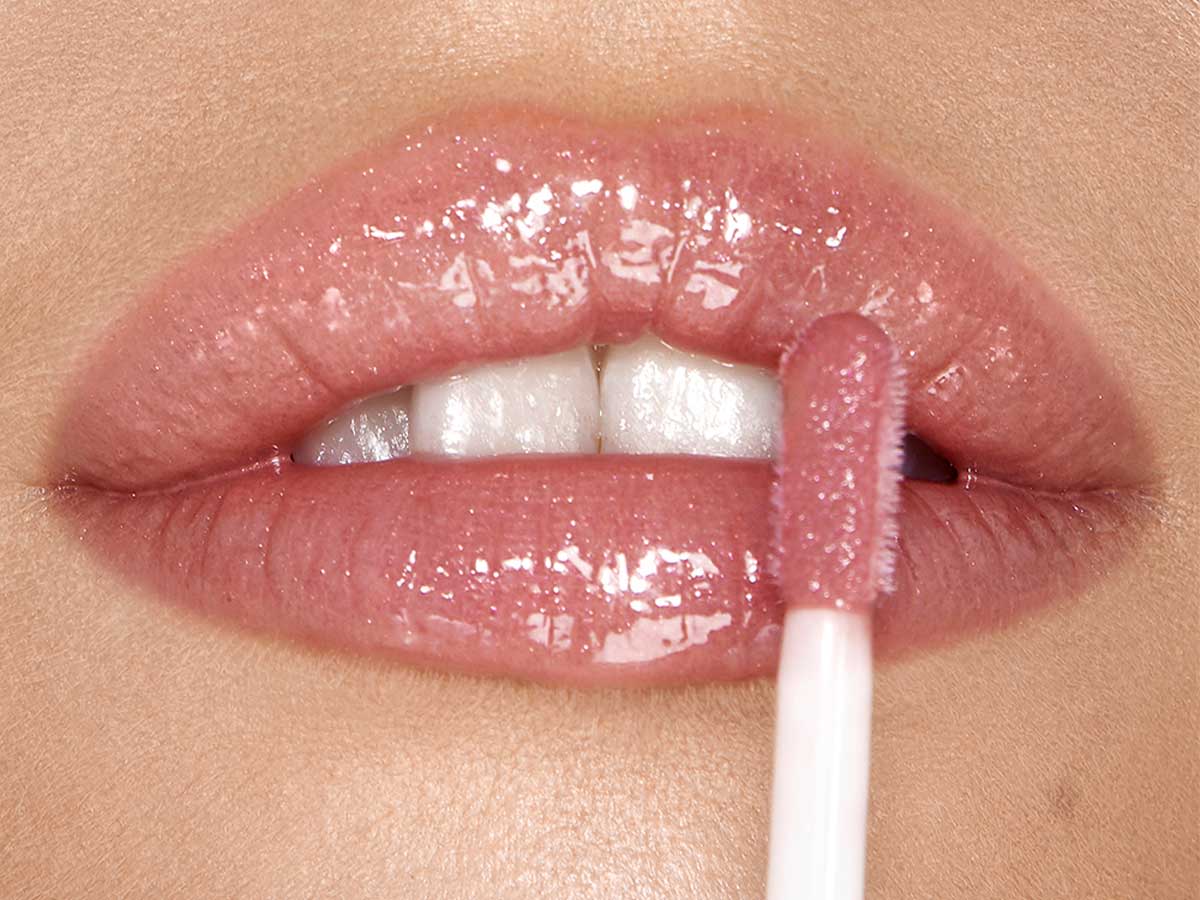 Jewel Lips in Pillow Talk on light-tone model Lips close-up of a light-tone model applying a nude pink lip gloss with a rose-golden sparkle.