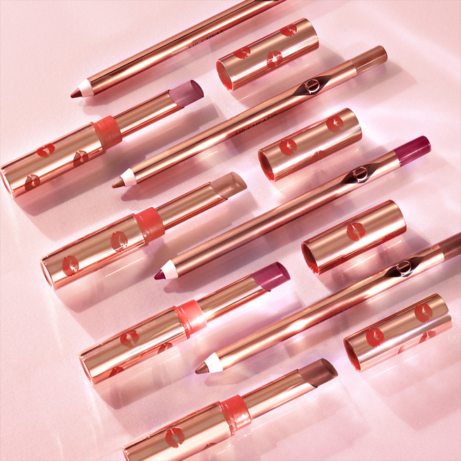 A collection of open lipsticks in shades of red, in gold-coloured tubes with red-coloured kiss prints all over and matching lip liner pencils. 