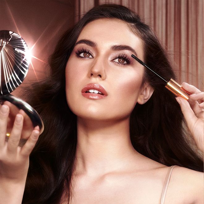 Fair-tone model with brown eyes applying mascara A fair-tone brunette model applying mascara while holding a powder compact in her other hand.