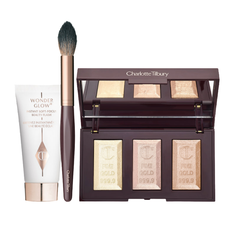 A face primer in white and white-gold packaging with a face blending brush in bronze and gold colour scheme and an open highlighter trio palette with powder highlighters in white-gold, rose-gold, and dark-gold shades. 