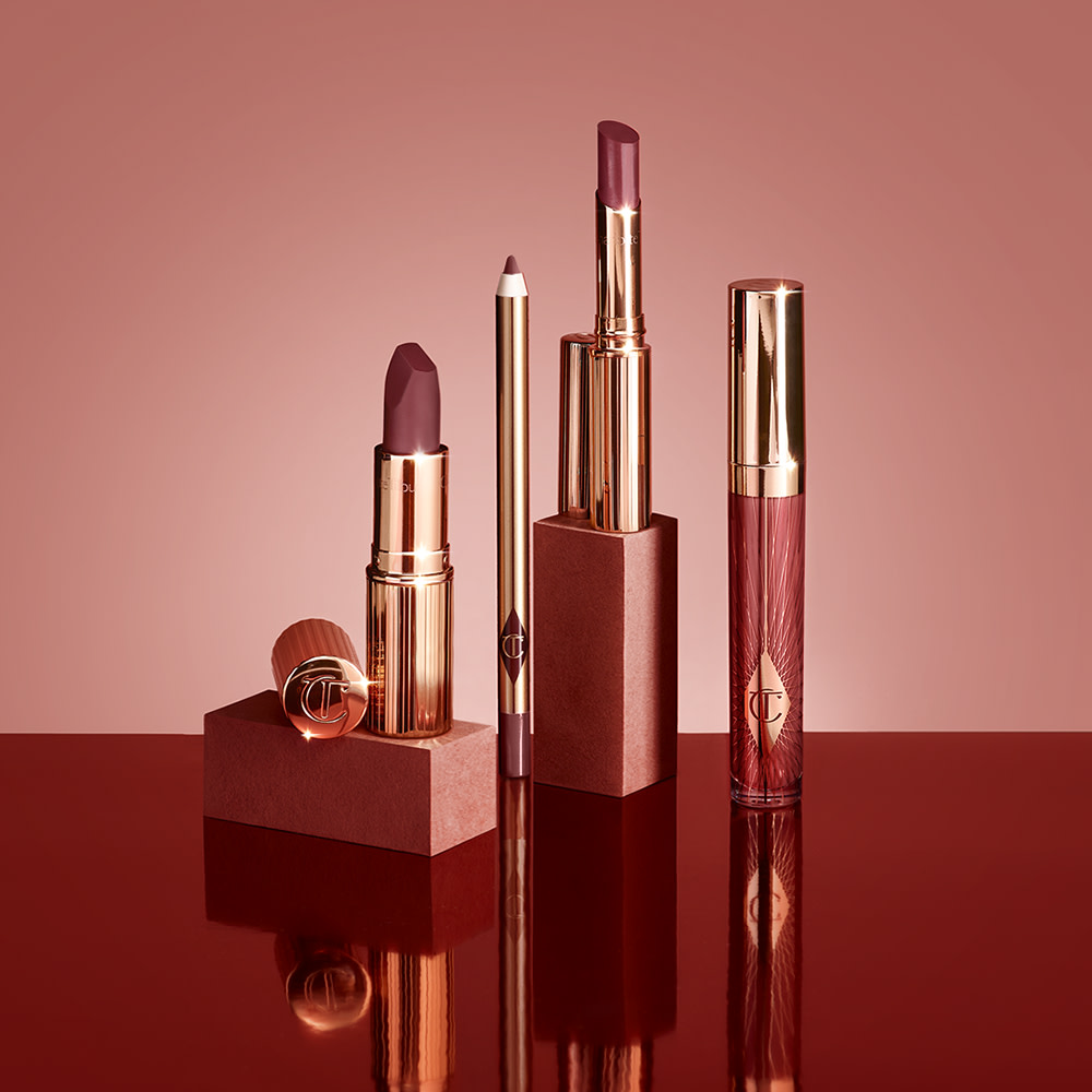 A collection of open lipsticks, lipstick lip balms, lip liner pencils, and lip glosses in a dark berry-rose shade. 
