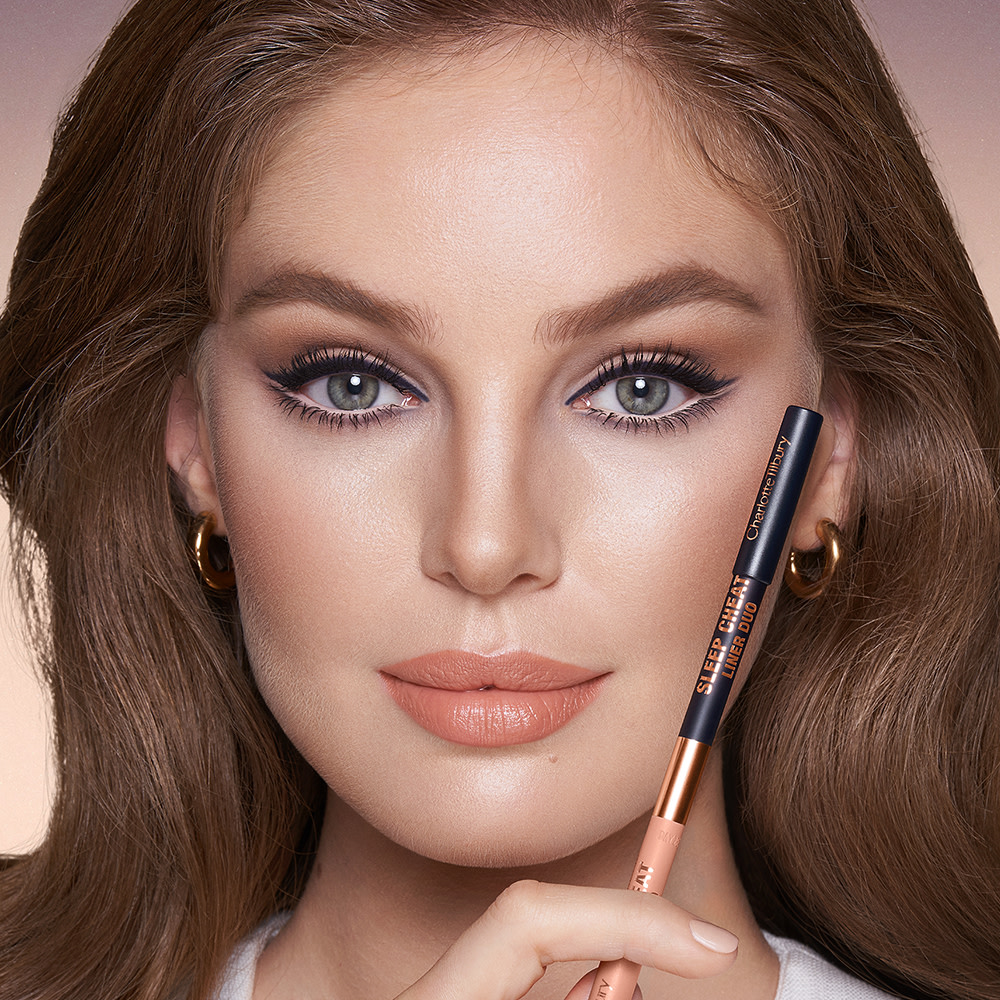Fair-tone model with blue eyes wearing jet-black eyeliner pencil on her eyelid and nude beige eyeliner pencil on her lower waterline with peach lipstick and subtle eye makeup.