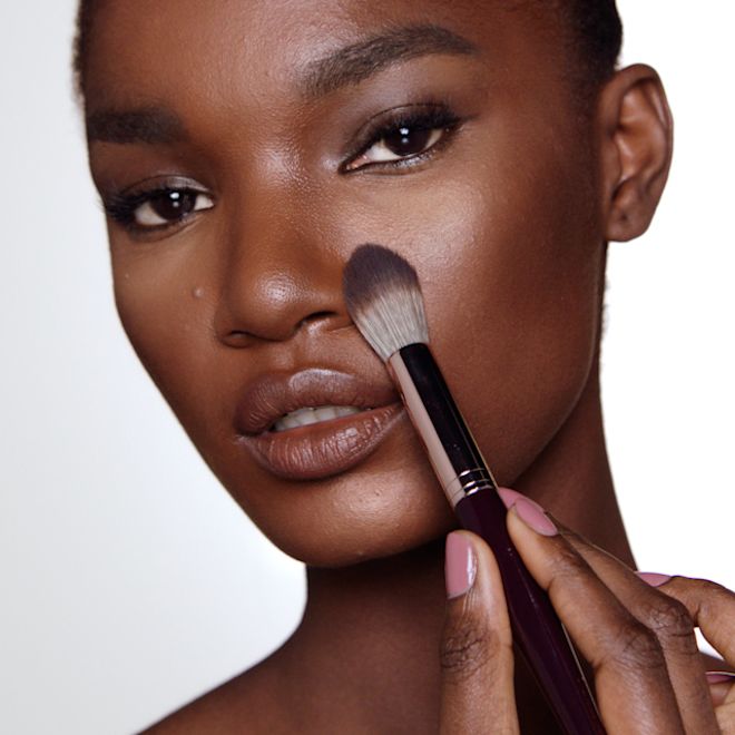 Brightening Airbrush Flawless Finish on deep-tone model A deep-tone model wearing glowy makeup and applying a radiant, setting powder that brightens, covers blemishes, and makes her skin look fresh.