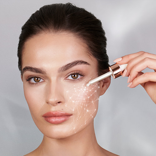 A light-tone brunette model applying a pearly-white, glowy face serum with a dropper. 