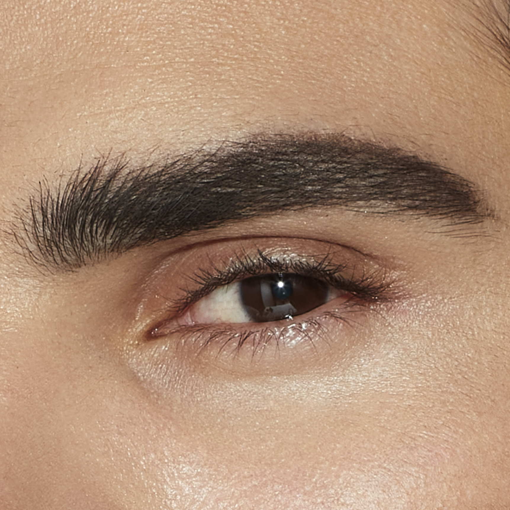 Single-eye close-up of a male model with brown eyes with shaped, lined, and filled-in brows in a black-brown colour that makes the eyebrows look full and lush.