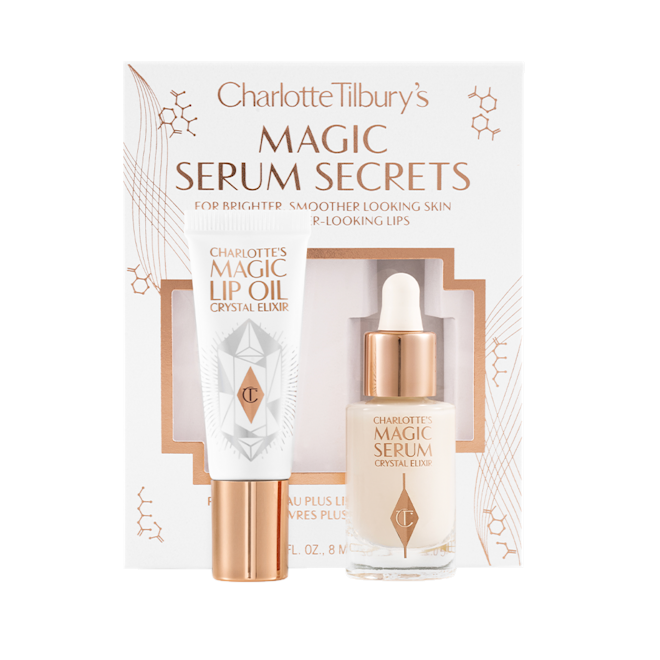 Magic Serum Secrets displayed with box Travel-size lip oil in a white-coloured tube with a gold-coloured lid and a mini, glow-enhancing serum in a glass bottle with a gold and white-coloured dropper lid with their packaging sleeve behind them in a white colour with the text, 'Magic serum secrets' written on it'