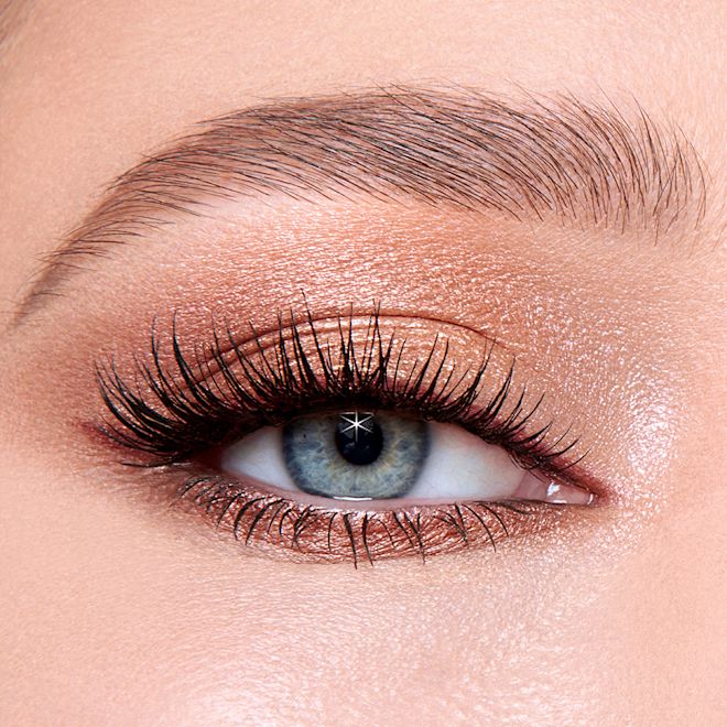 Luxury Palette of Pops in Celestial Eyes on blue eye close-up Single-eye close-up of a fair-tone model with blue eyes wearing shimmery fawn, gold, and brown eyeshadow with brown eyeliner and lengthening mascara.