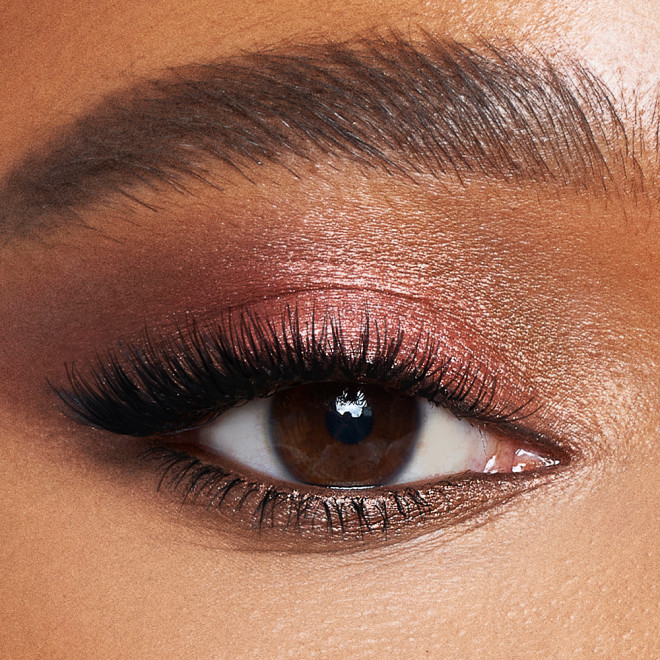 Single-eye close-up of a deep-tone model with brown eyes with shimmery rose gold and brown eye makeup. 