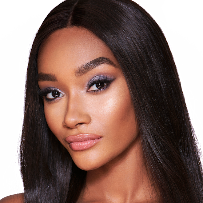 The Uptown Girl look on deep-tone model A deep-tone blonde model with brown eyes wearing shimmery lilac and champagne eye makeup with nude pink blush and a warm, coral lipstick.