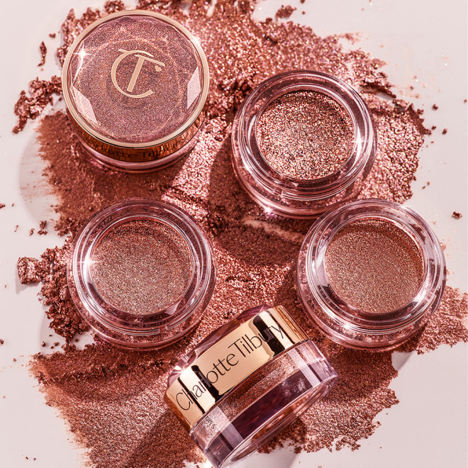 A collection of eyeshadow pigment in berry-pink shade in glass pots with gold-coloured lids.