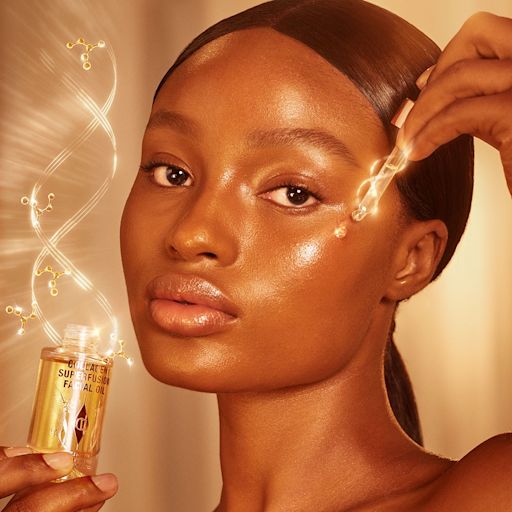 Collagen Superfusion Facial Oil on deep-tone model deep-tone model with glowy, luminous, glass skin, applying a light-gold-coloured facial oil from a glass bottle with a gold and white-coloured dropper lid.