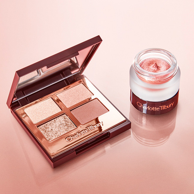 An open, mirrored-lid quad eyeshadow palette in shades of pink, gold, and brown with cream eyeshadow in a glass pot in a rose gold shade.