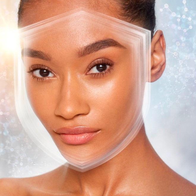 Deep-tone brunette model wearing a smoothing primer with a satin-finish with an illusion of a shield over her face to depict protection from UV rays.