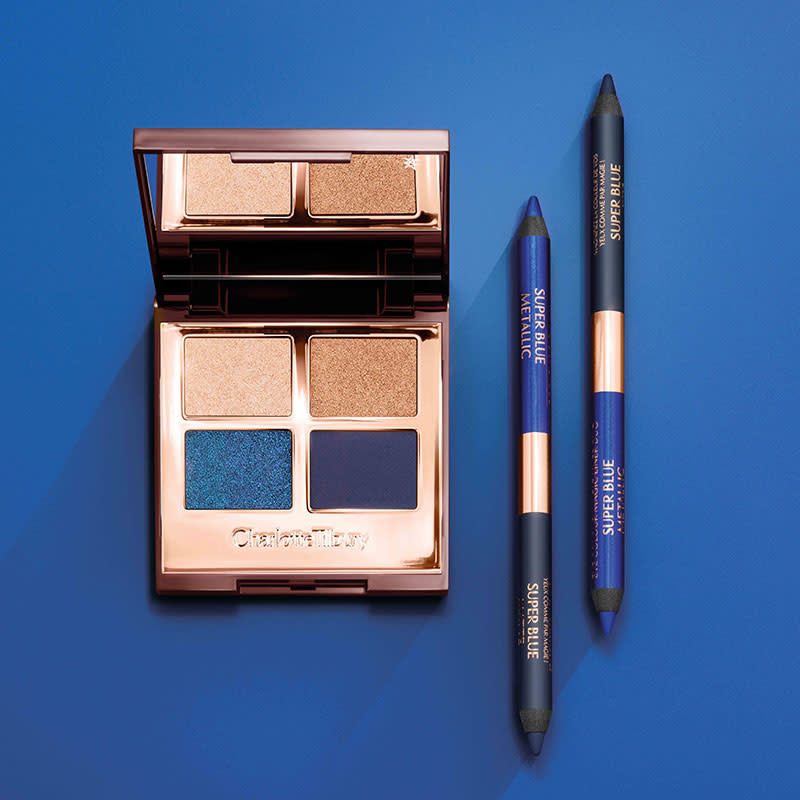 An open, mirrored-lid quad eyeshadow palette with shimmery and matte eyeshadows in shades of blue and gold, and double-sided, identical eyeliners in emerald blue and teal. 