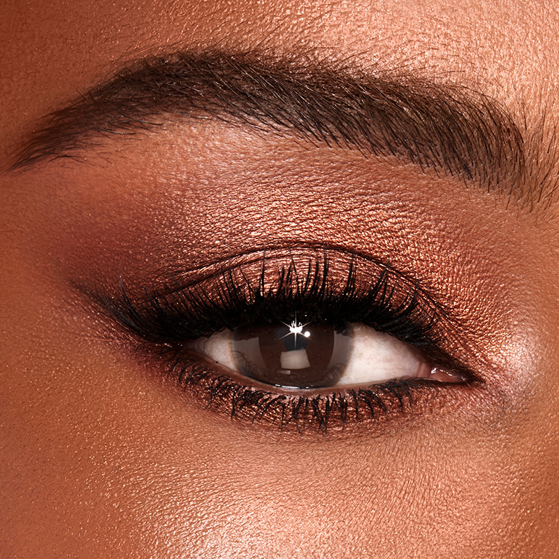 Single-eye close-up of a deep-tone model with brown eyes wearing shimmery brown and gold eyeshadow. 