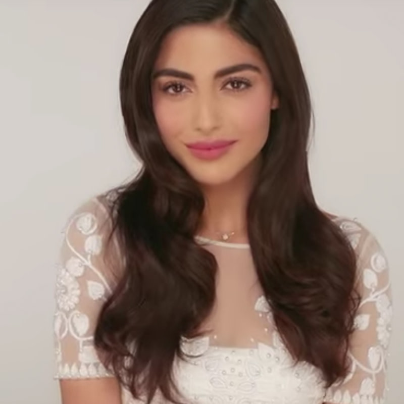 A medium-tone model wearing a cool-toned pink lipstick with glowy, nude makeup, that's a recreation of Amal Clooney's wedding makeup look.