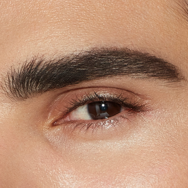 Single-eye close-up of a male model with brown eyes and thick, shaped, and filled eyebrows in a blac-brown colour.