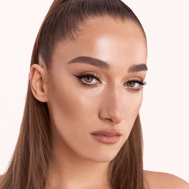 Light-tone model with brown eyes wearing soft beige and champagne eyeshadow with black eyeliner on her eyelid and nude beige eyeliner on her lower waterline along with a muted rose nude lipstick.
