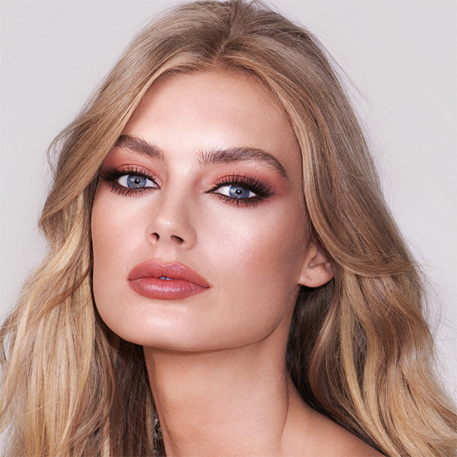 Close-up of a fair-tone model with blue eyes wearing a nude brown-peach lipstick with eye makeup in shimmery and matte pink, terracotta, and brown shades.