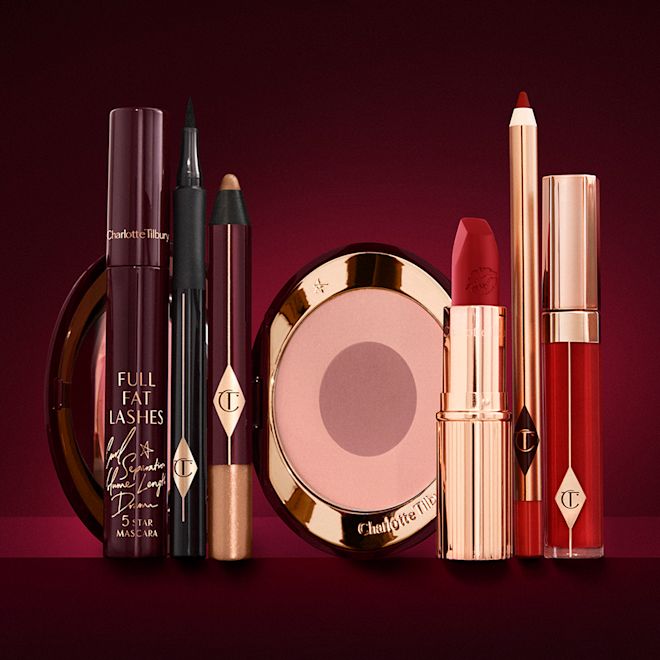 The Bombshell Deep Look kit displayed An open two-tone blush in cool-toned pink and brown with a mascara, eyeliner pen, chubby eyeshadow stick in gold, an open lipstick in bold red, lip liner pencil in blood-red, and a lip gloss in bright red.
