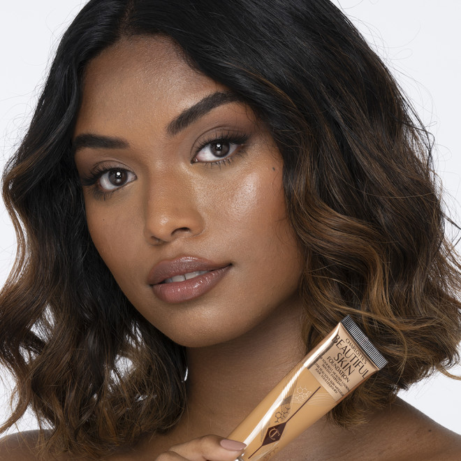 Dark-tone brunette model wearing glowy, skin-like foundation with a satin finish with nude lipstick and subtle eye makeup.