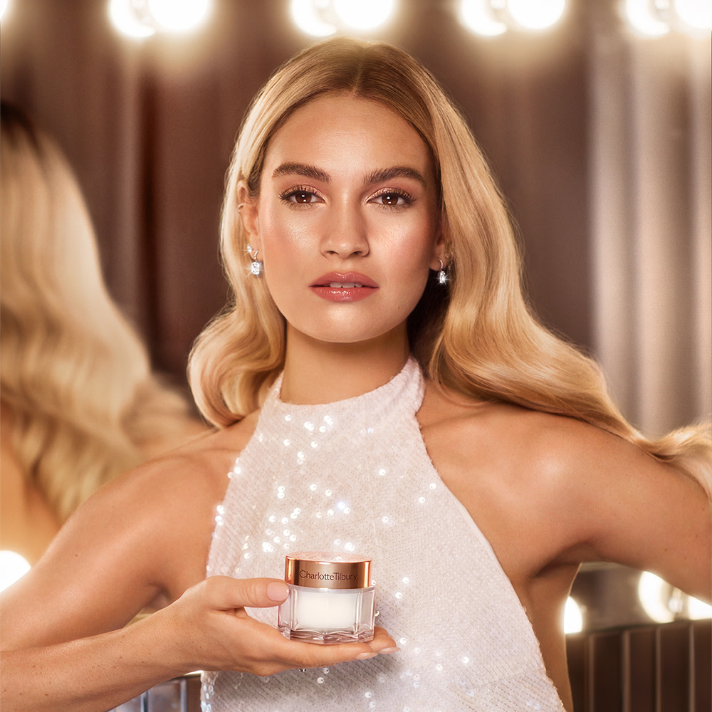 Pearly-white face cream in a glass jar with a gold-coloured lid held by actress Lily James. 