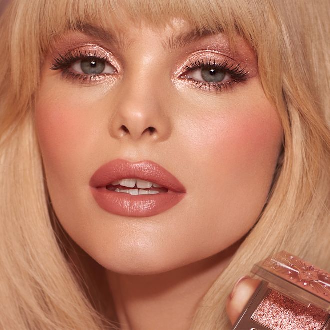 Megan wearing and holding Pillow Talk Hypnotising Pop Shot in Diamond Dimension A fair skin blonde model wearing a shimmery pink eyeshadow