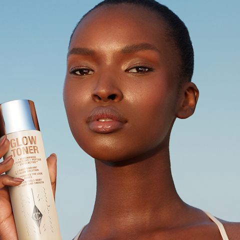 Deep-tone model with glowing, fresh skin holding a large toner bottle filled with a creamy, silvery-white-coloured toner with a silver-coloured lid.