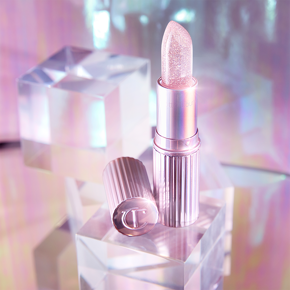 An open glittery, colour-changing lipstick in a sheer pink colour with a luminous purple-coloured tube and lid. 