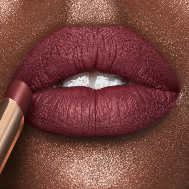 Lips close-up of a deep-tone model wearing rosewood red lipstick with a matte finish.