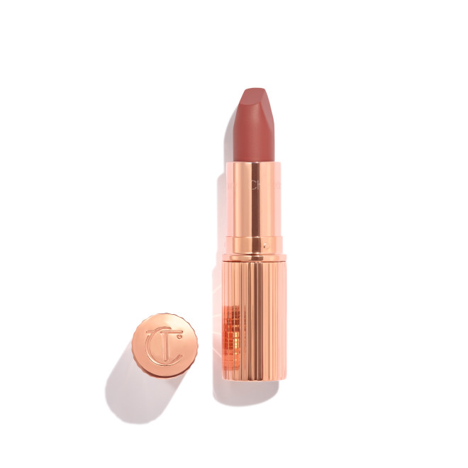 Opened, berry-pink lipstick in a metallic, golden case with its lid that's embossed with CT placed next to it. 