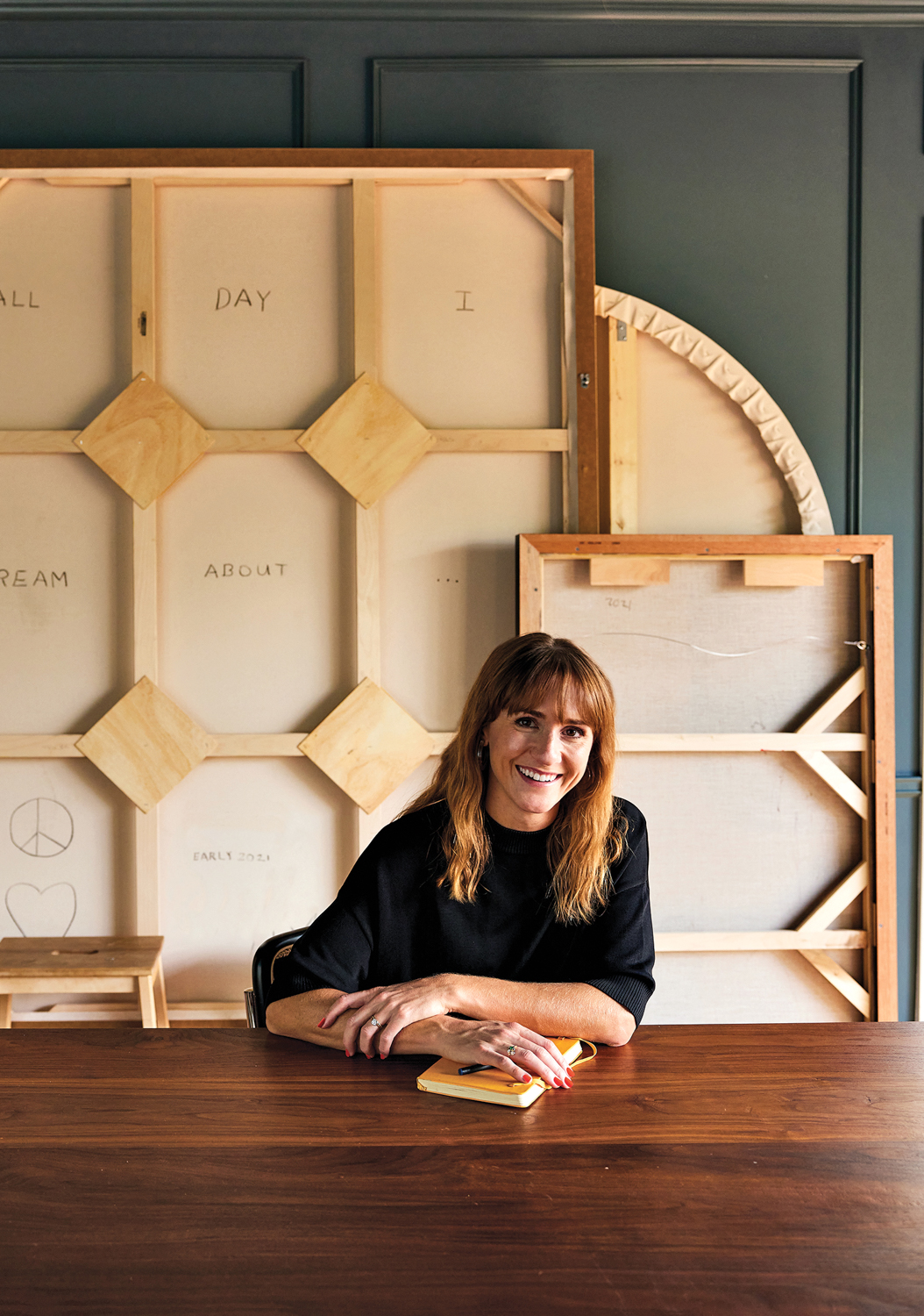 Keli Hogsett sitting at a large wood table with the backs of several art canvases behind her.