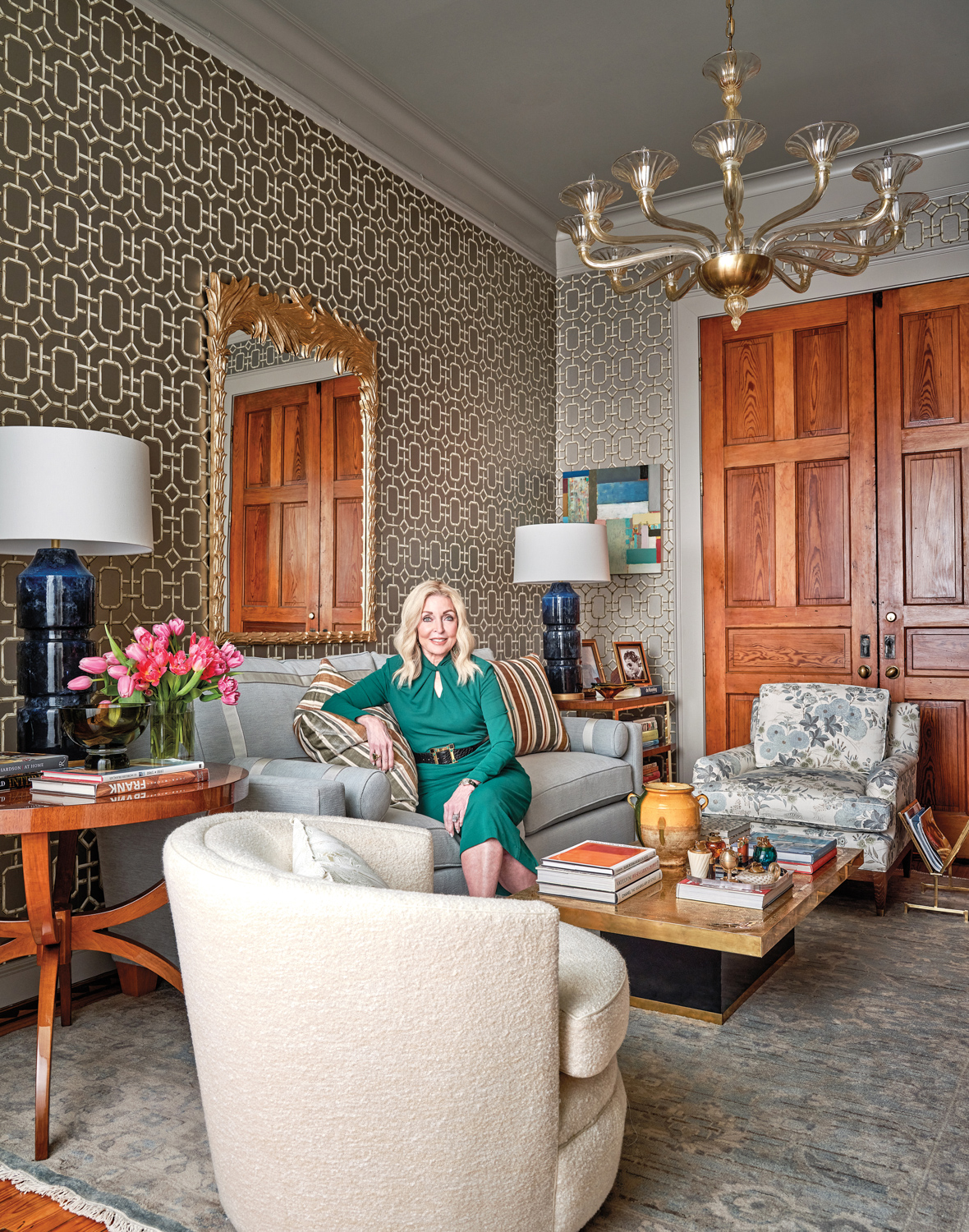 Jan Showers in a green dress sitting on a gray sofa with a metallic geometric wallcovering behind.