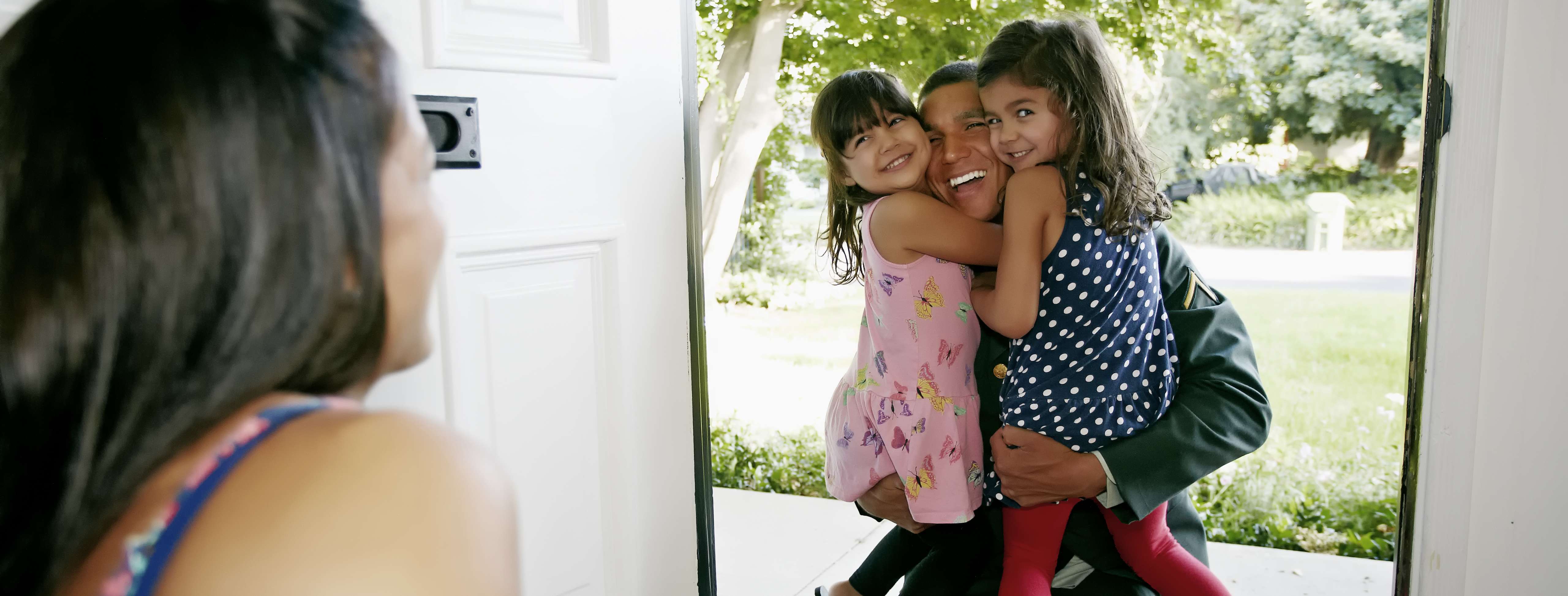 Child care provider smiling while military father hugs his children.