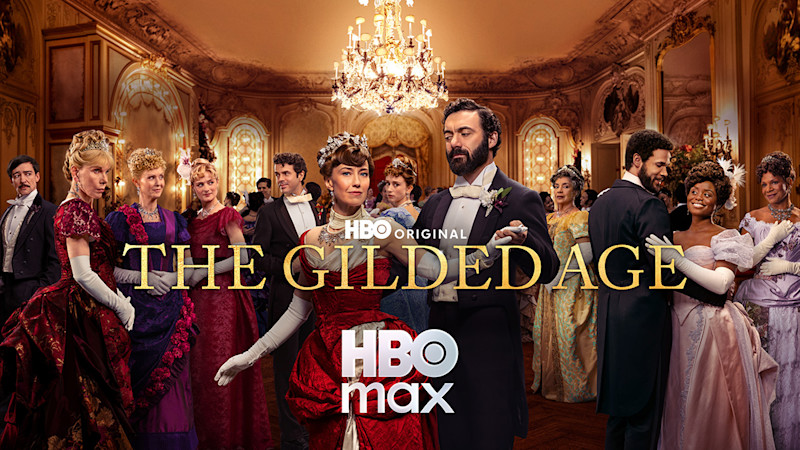 Skådespelare i eleganta 1800-talskläder i en lyxig balsal med kristallkrona, från HBO-serien "The Gilded Age".