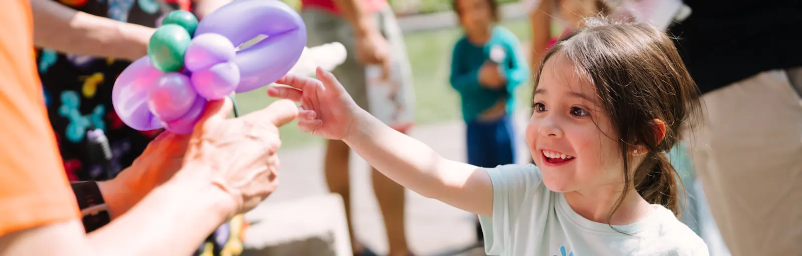 Youth reaching for balloon art at the Flint Hills Family Festival 2025. Photo by Laura Alpizar.