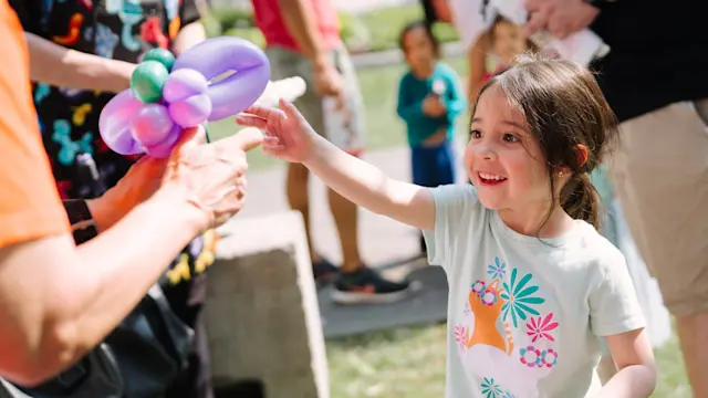 Youth reaching for balloon art at the Flint Hills Family Festival 2025. Photo by Laura Alpizar.