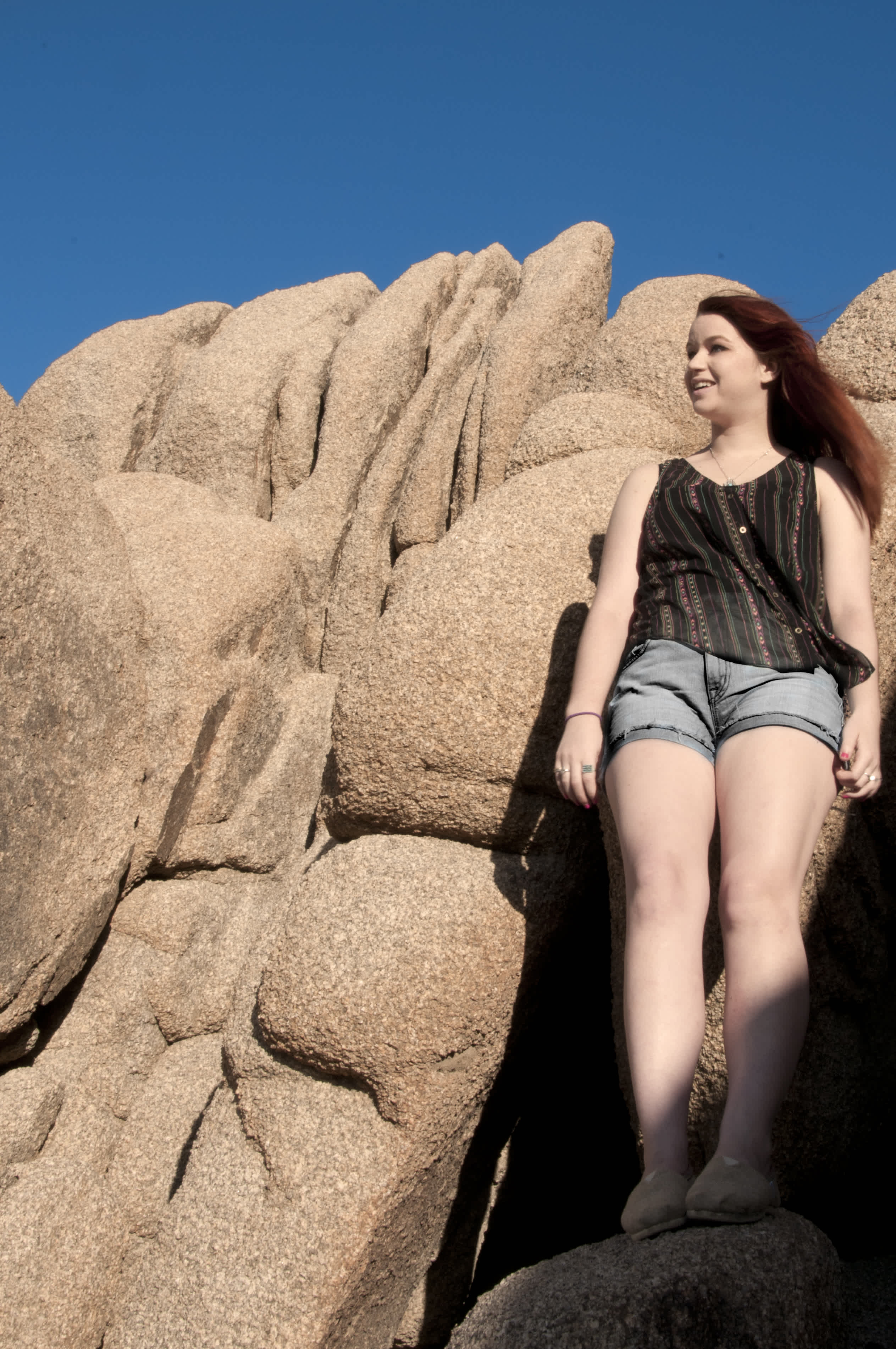 Girl in shorts standing against a pile of boulders.
