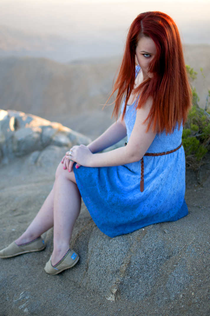 Girl in a blue dress with red hair sitting on a boulder. 