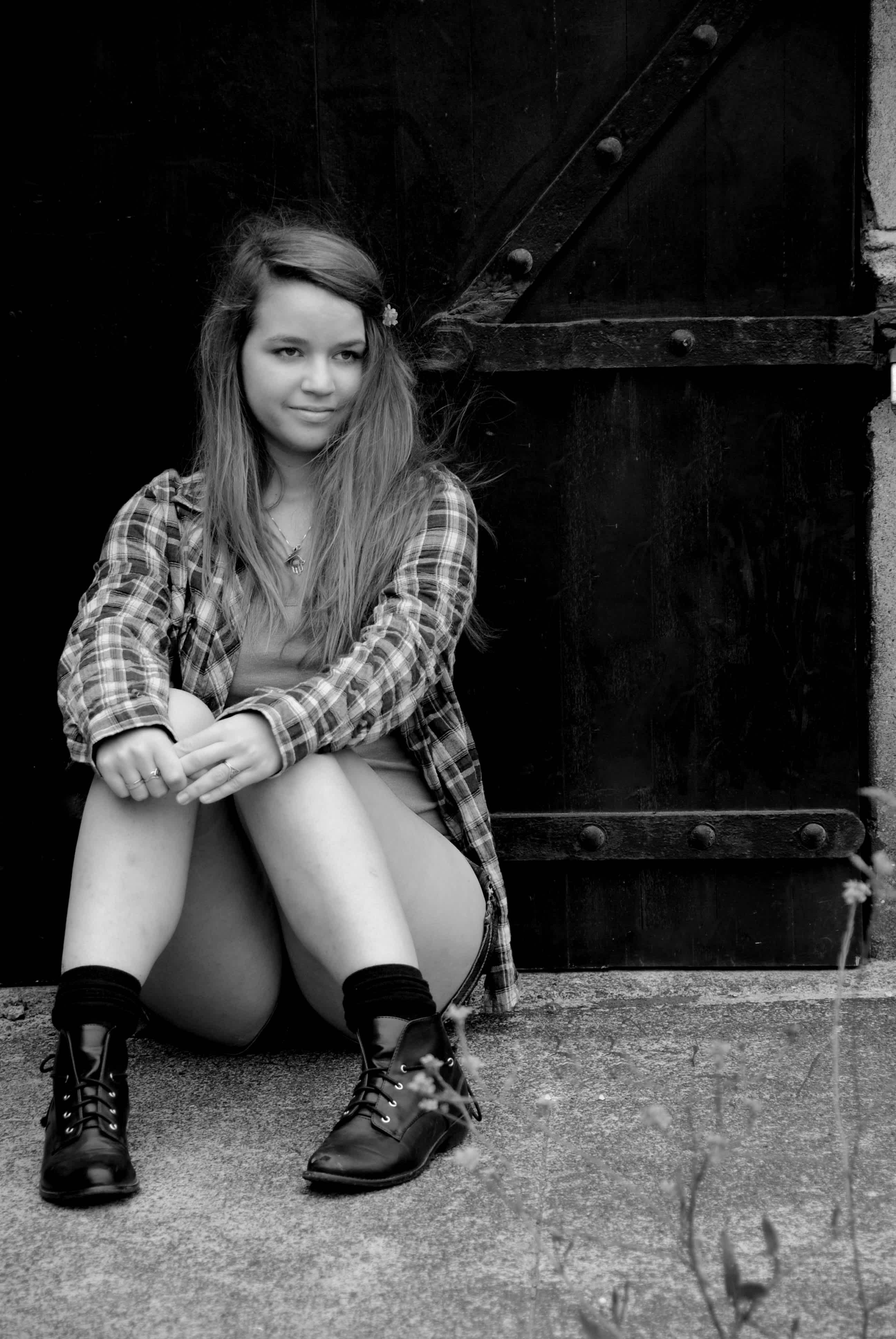 Black and white girl in plaid sitting against a gate. 