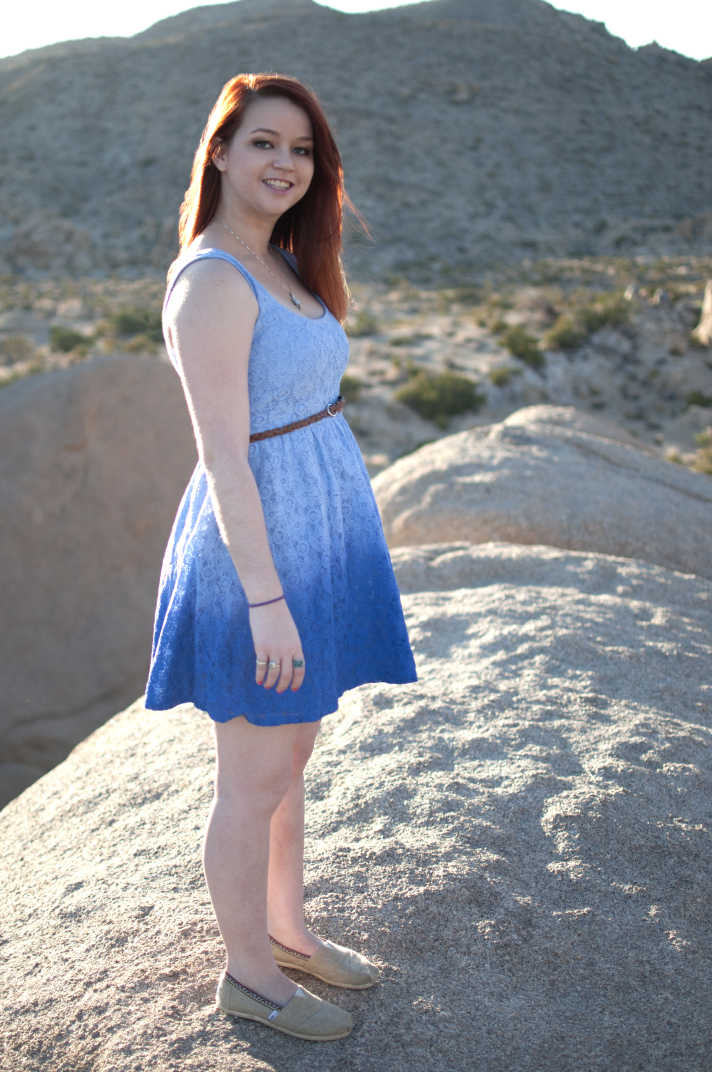 Girl in a blue dress standing in front of a mountain backdrop. 