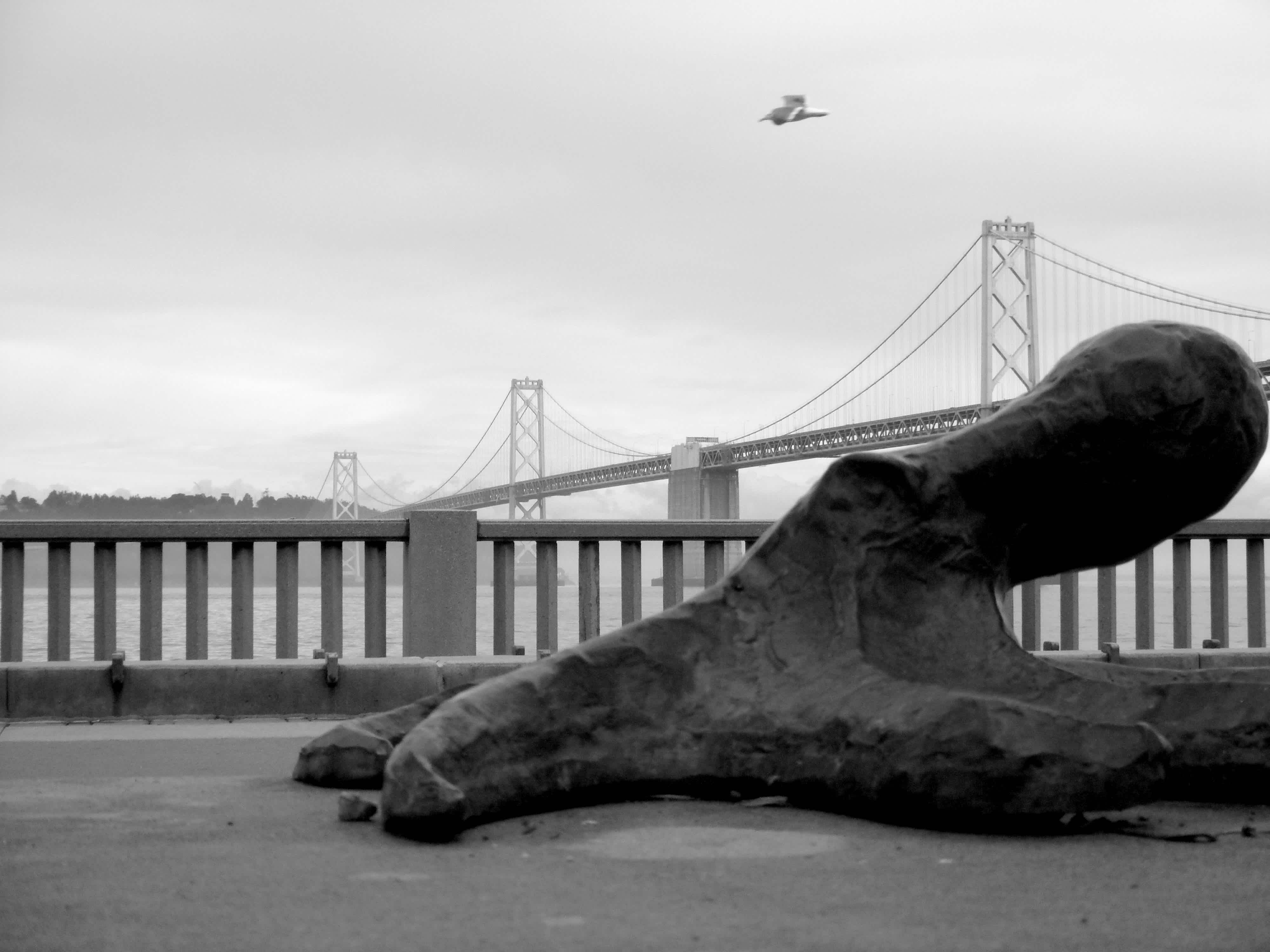 Statue in front of a railing with a bridge in the background in black and white in Ferry Building, San Francisco, California. 