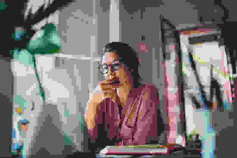 Woman with glasses looking at a laptop and pondering