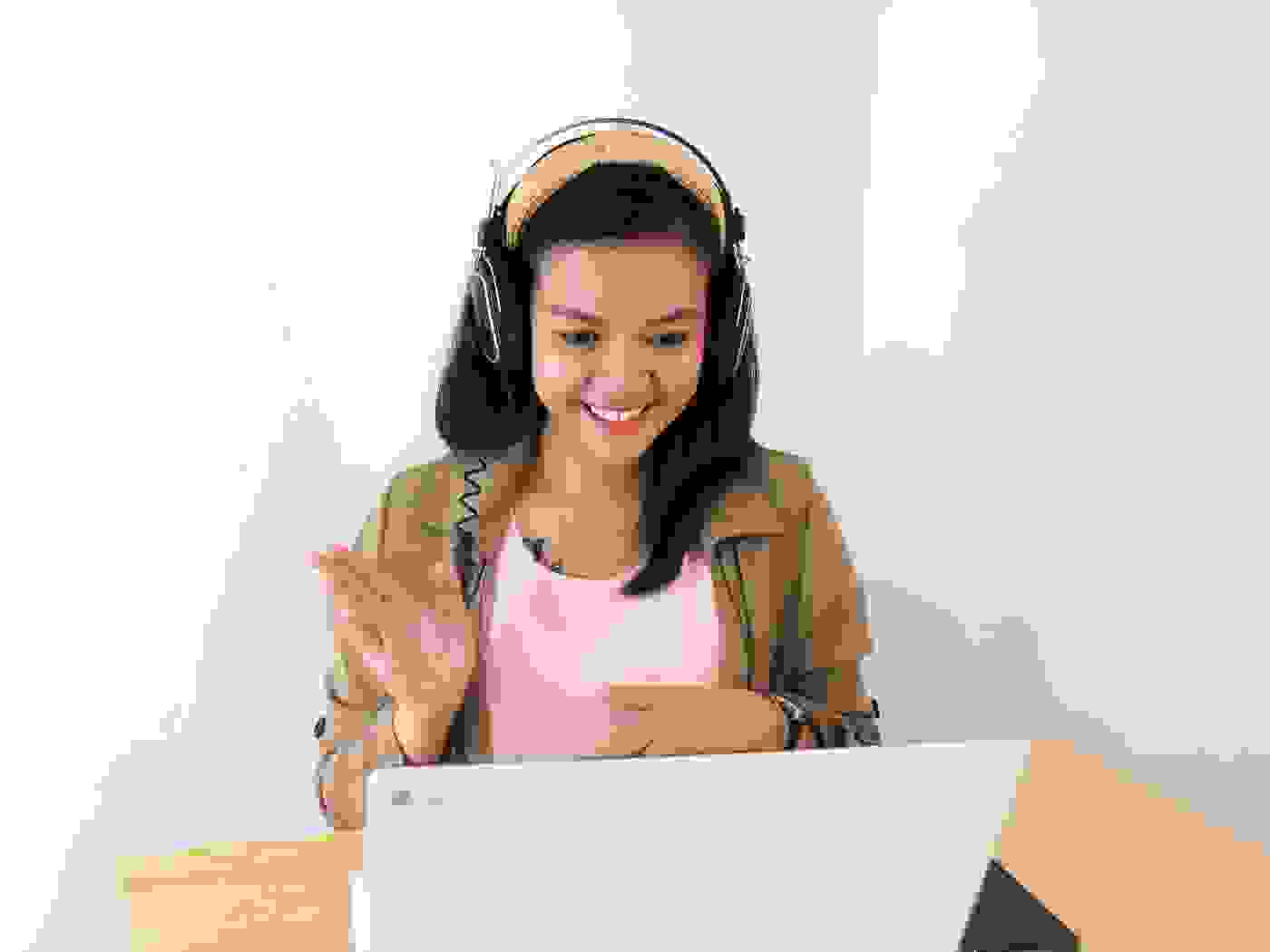 Brown-haired woman waving at a computer screen.