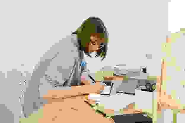 A person sits at their desk taking notes in front of their laptop. Photo by Ivan Samkov.