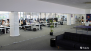 Inside of an office with white walls and a large glass divider showing a sofa, ping pong table, and many people busy at work sitting at desks