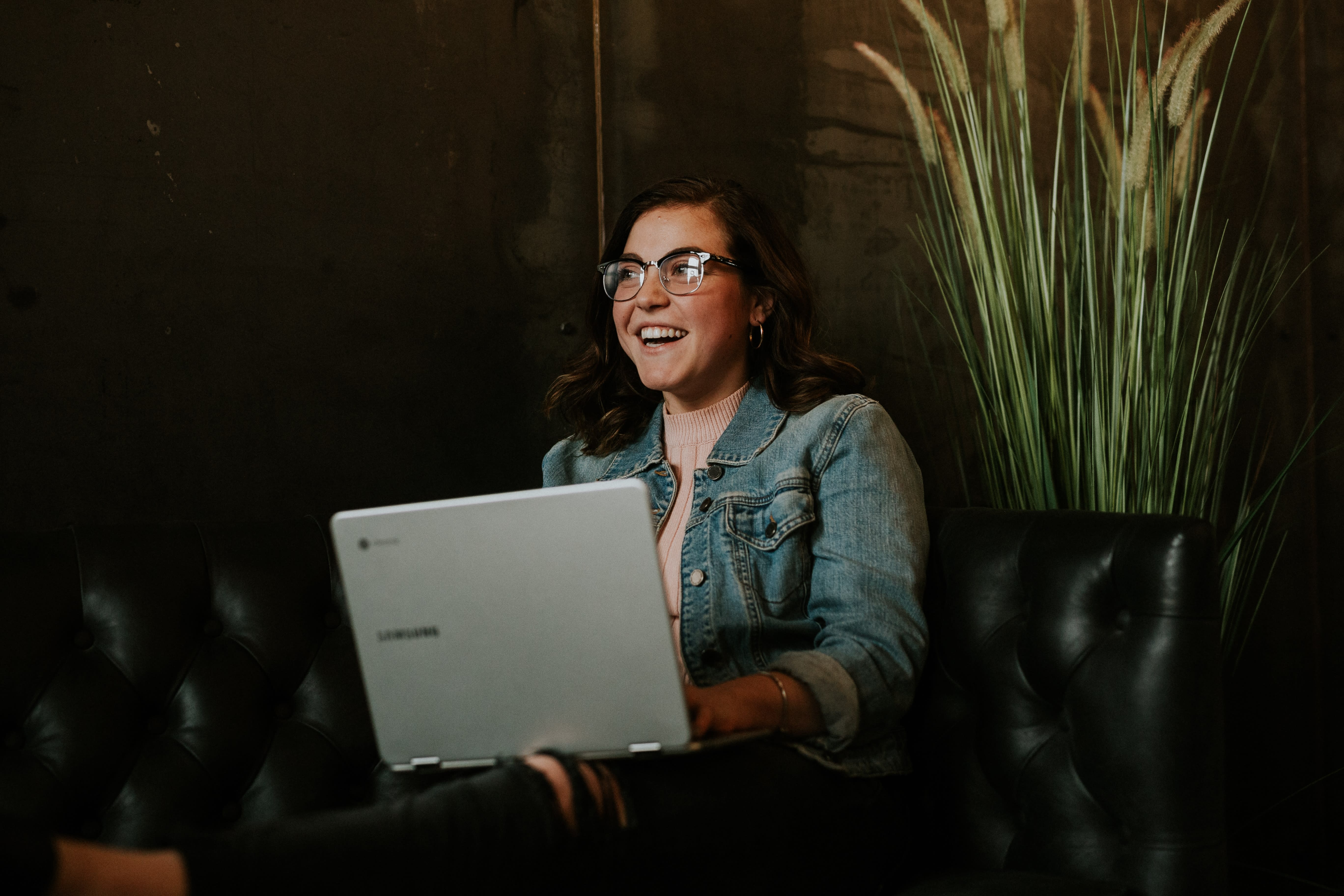 Woman sat on a sofa with a laptop laughing