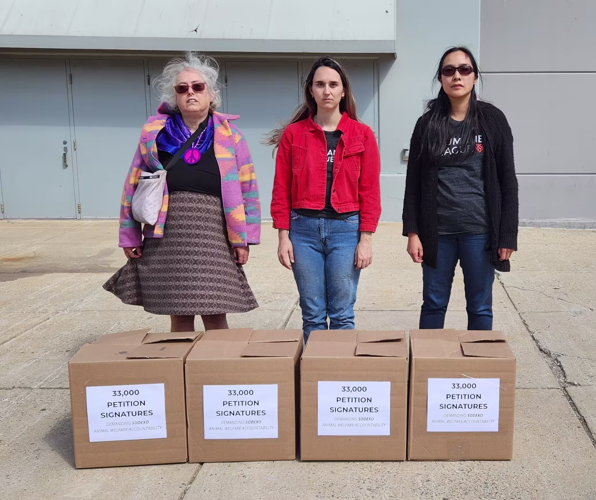 Three activists stand behind four large cardboard boxes of petition signatures.