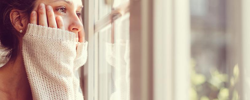 Feature image - Defamation Woman holding her face looking out the window