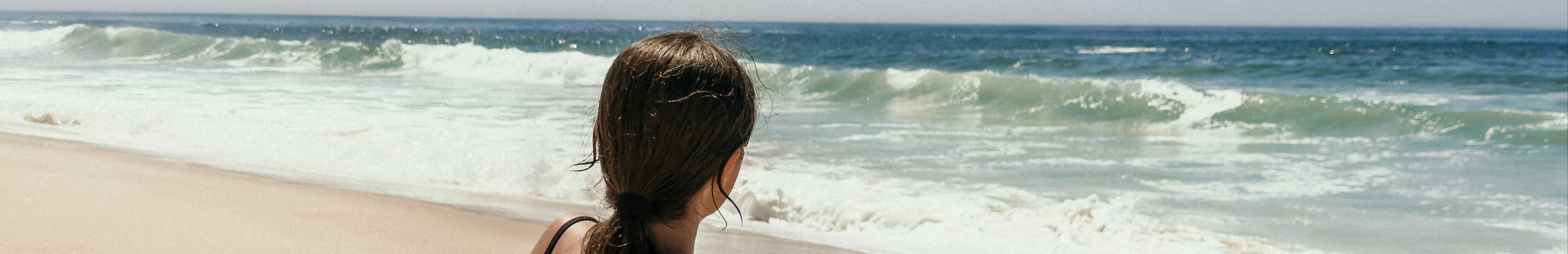 Femme en maillot de bain, vue de dos, assise face à la mer.